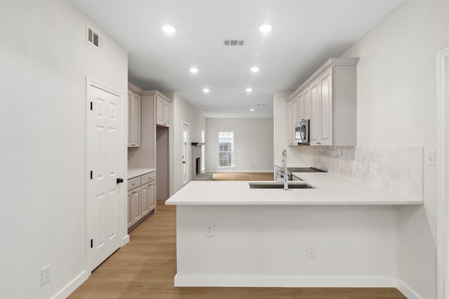 kitchen featuring kitchen peninsula, decorative backsplash, light hardwood / wood-style flooring, and sink