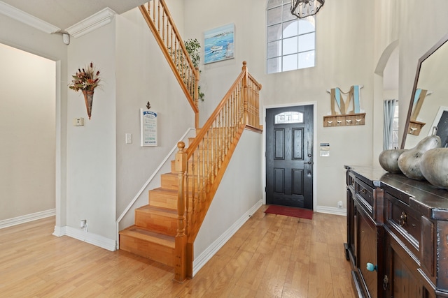 foyer featuring light hardwood / wood-style floors, ornamental molding, and a towering ceiling