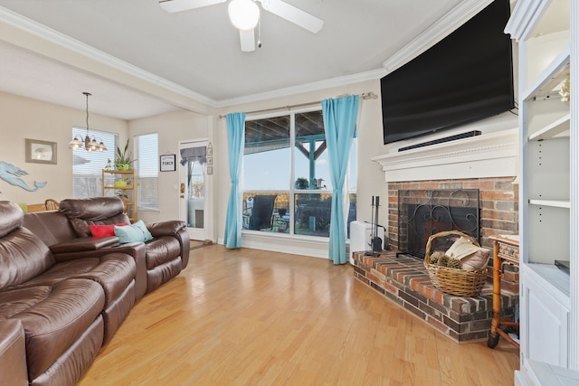 living room featuring ceiling fan with notable chandelier, light wood-type flooring, a fireplace, and ornamental molding