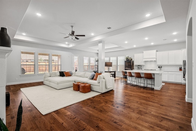 living room with dark wood-type flooring, ceiling fan, and a raised ceiling