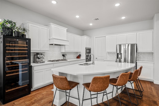 kitchen featuring sink, stainless steel appliances, premium range hood, an island with sink, and white cabinets