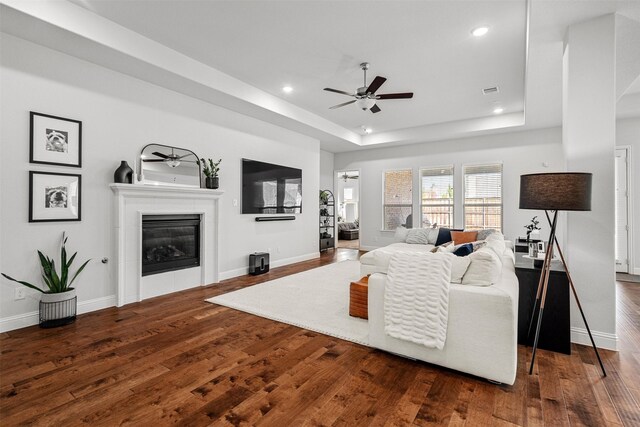 living room with ceiling fan, dark hardwood / wood-style flooring, a raised ceiling, and a tile fireplace