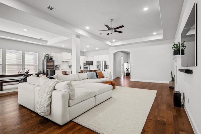 living room featuring a tray ceiling, ceiling fan, and dark hardwood / wood-style floors