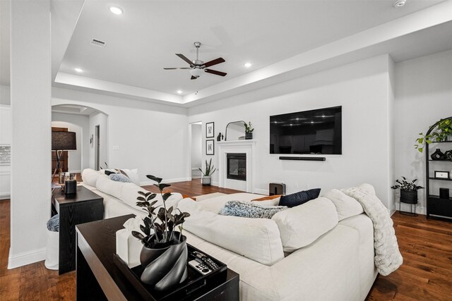 living room with ceiling fan, dark hardwood / wood-style flooring, and a tray ceiling