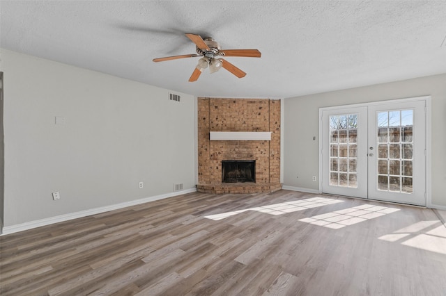 unfurnished living room with french doors, a brick fireplace, hardwood / wood-style flooring, ceiling fan, and a textured ceiling