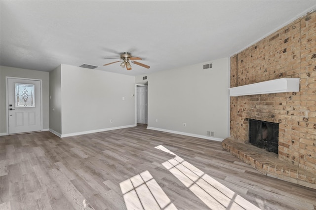 unfurnished living room featuring light wood-type flooring, a brick fireplace, and ceiling fan