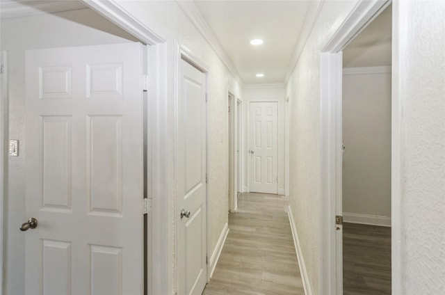 hallway featuring baseboards, a textured wall, crown molding, light wood-style floors, and recessed lighting