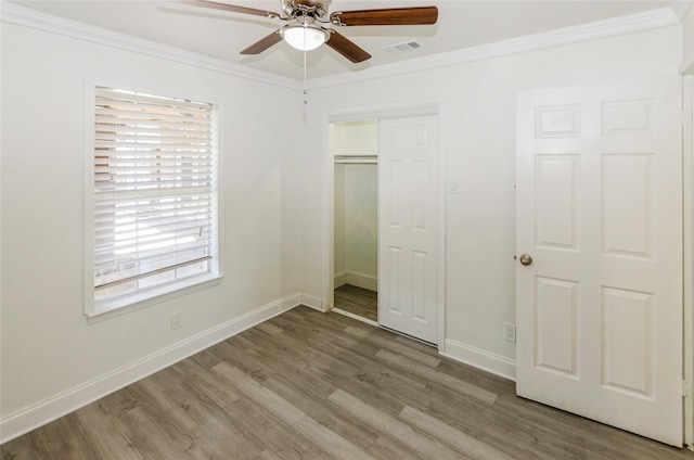 unfurnished bedroom with wood finished floors, visible vents, baseboards, a closet, and crown molding