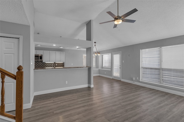 unfurnished living room with ceiling fan with notable chandelier, a textured ceiling, dark hardwood / wood-style flooring, and high vaulted ceiling