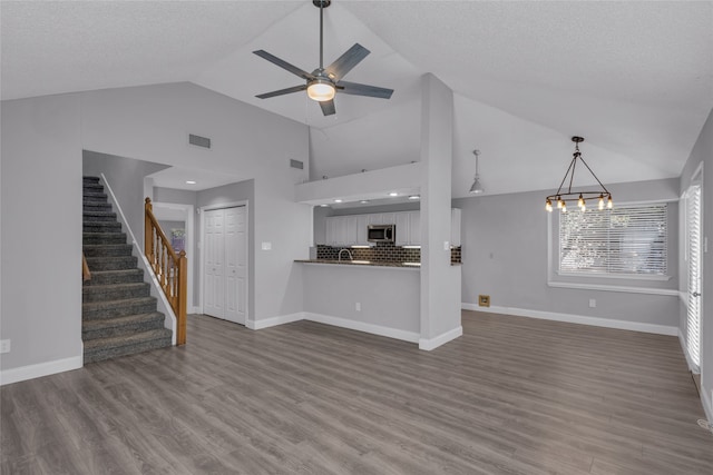 unfurnished living room with a textured ceiling, dark hardwood / wood-style flooring, high vaulted ceiling, and ceiling fan