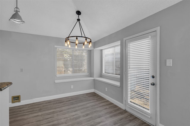 unfurnished dining area featuring hardwood / wood-style floors, a textured ceiling, and an inviting chandelier