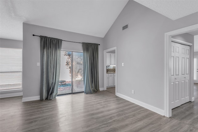 spare room with a textured ceiling, high vaulted ceiling, and light hardwood / wood-style flooring