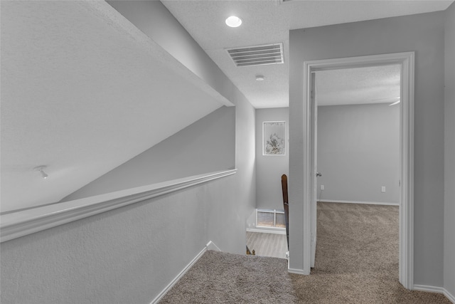 stairway featuring lofted ceiling, carpet floors, and a textured ceiling