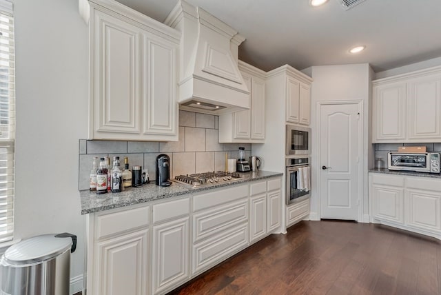 kitchen featuring dark wood-type flooring, appliances with stainless steel finishes, white cabinetry, light stone counters, and custom exhaust hood