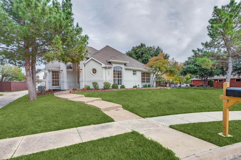 view of front of house featuring a front lawn, a shingled roof, fence, and brick siding