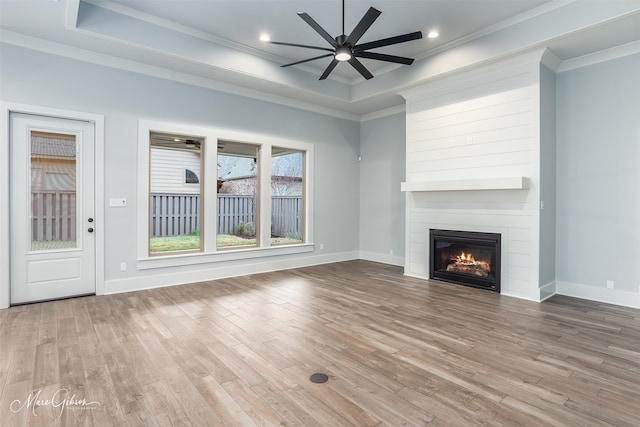 unfurnished living room featuring ornamental molding, a tray ceiling, hardwood / wood-style flooring, ceiling fan, and a fireplace