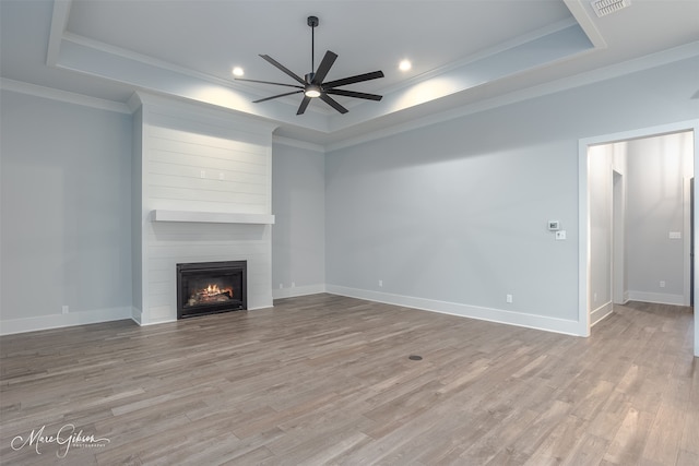 unfurnished living room featuring a raised ceiling, ornamental molding, a fireplace, and light hardwood / wood-style flooring