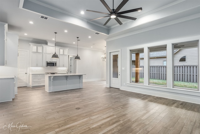 kitchen with decorative light fixtures, white cabinets, crown molding, a center island with sink, and light wood-type flooring