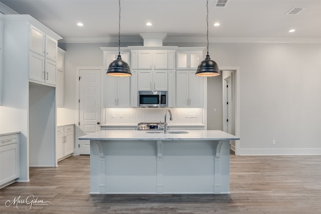 kitchen featuring hanging light fixtures, sink, a center island with sink, and white cabinets