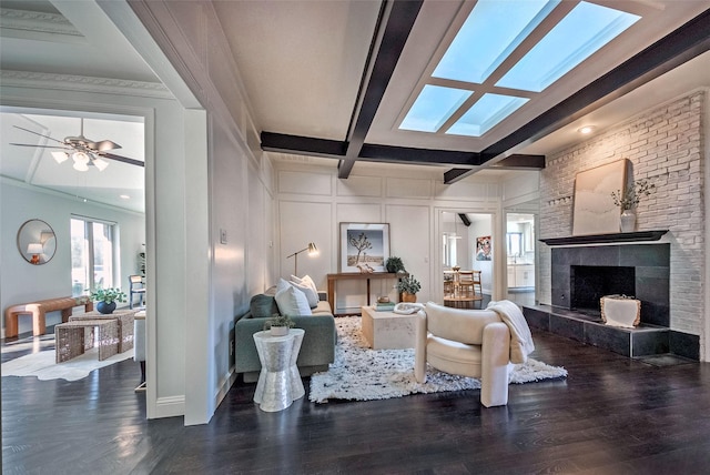 living room with beam ceiling, a skylight, dark hardwood / wood-style flooring, and a fireplace