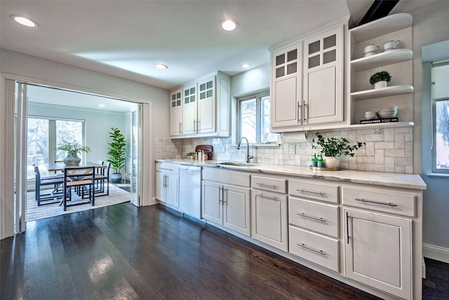 kitchen with tasteful backsplash, dishwasher, sink, white cabinetry, and light stone countertops