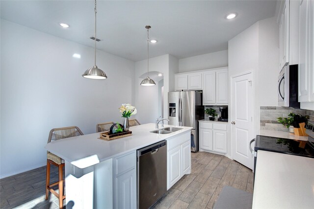 kitchen with a breakfast bar, a center island with sink, white cabinets, decorative light fixtures, and stainless steel appliances