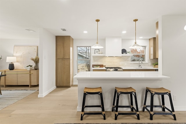 kitchen with custom exhaust hood, backsplash, sink, light wood-type flooring, and decorative light fixtures