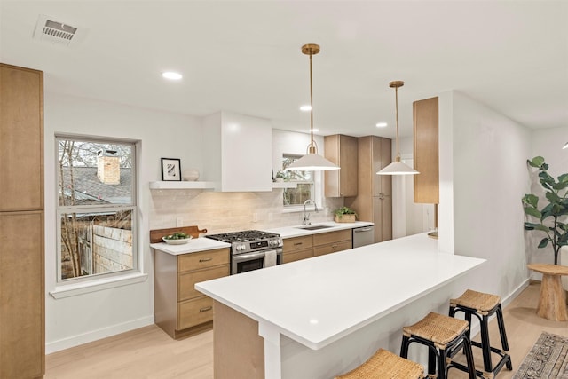 kitchen featuring kitchen peninsula, stainless steel appliances, sink, decorative light fixtures, and a breakfast bar area