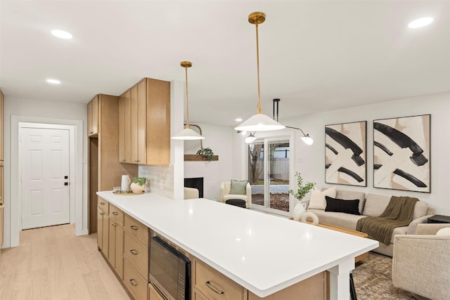 kitchen featuring black microwave, hanging light fixtures, backsplash, light hardwood / wood-style floors, and light brown cabinetry