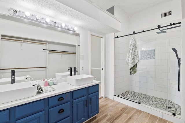 bathroom with a textured ceiling, vanity, wood-type flooring, and tiled shower