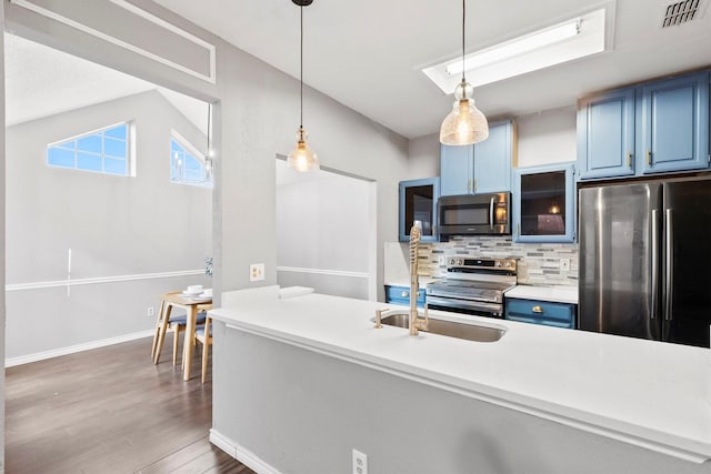 kitchen featuring stainless steel appliances, blue cabinets, hardwood / wood-style floors, vaulted ceiling, and decorative backsplash