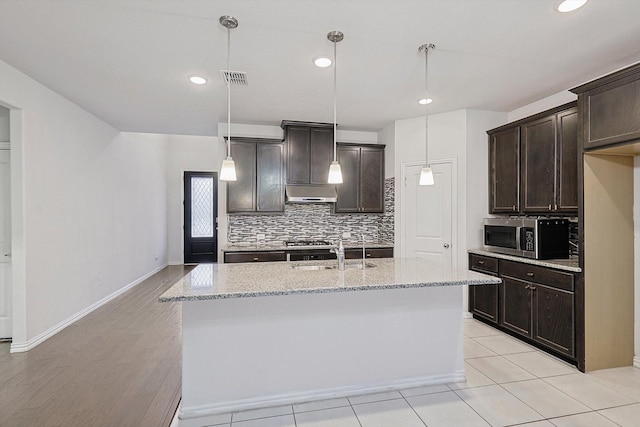 kitchen with dark brown cabinets, an island with sink, stainless steel appliances, and decorative light fixtures