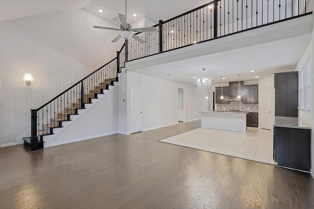 unfurnished living room with high vaulted ceiling, light hardwood / wood-style floors, and ceiling fan with notable chandelier