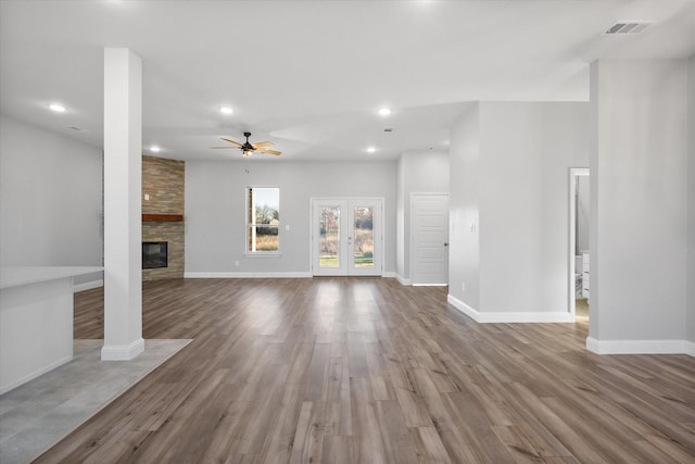 unfurnished living room with french doors, a large fireplace, wood-type flooring, and ceiling fan