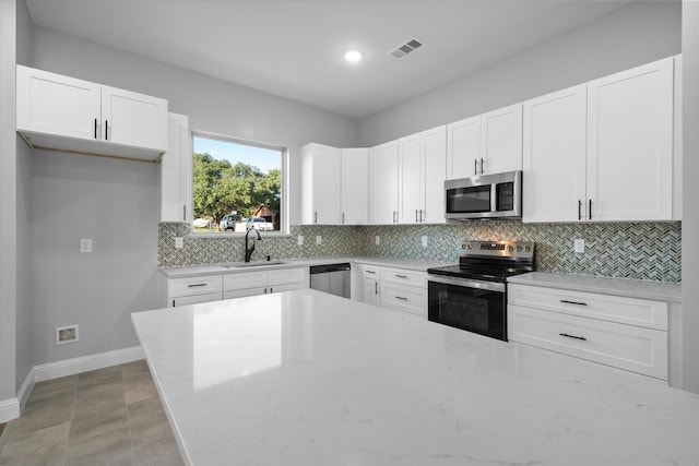 kitchen featuring sink, appliances with stainless steel finishes, white cabinetry, light stone counters, and decorative backsplash