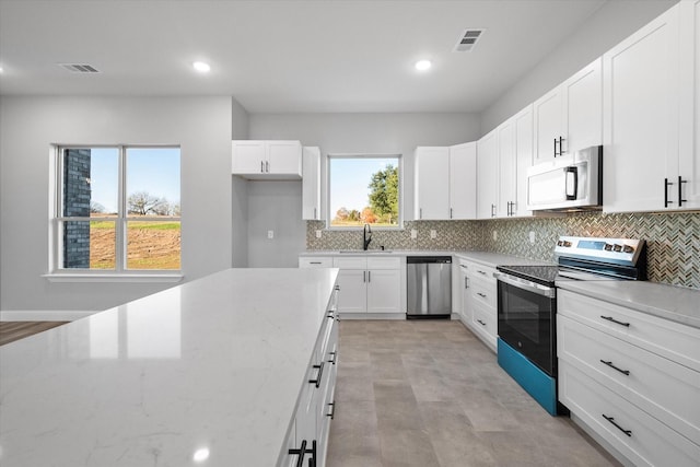 kitchen with sink, white cabinetry, stainless steel appliances, light stone countertops, and decorative backsplash