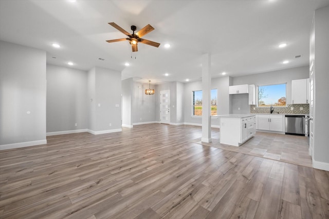 unfurnished living room featuring sink, ceiling fan with notable chandelier, and light hardwood / wood-style flooring