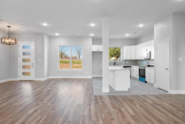 kitchen with tasteful backsplash, white cabinets, hanging light fixtures, stainless steel appliances, and light wood-type flooring