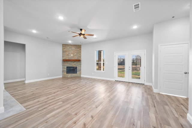 unfurnished living room featuring a fireplace, light hardwood / wood-style floors, french doors, and ceiling fan