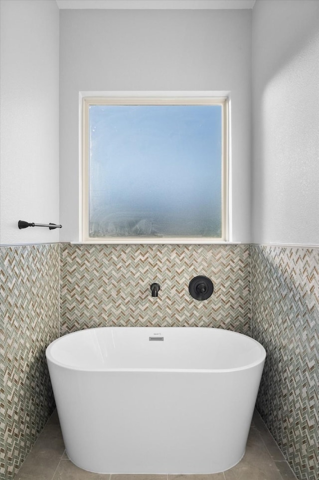 bathroom with tile patterned flooring, a bath, tile walls, and a healthy amount of sunlight