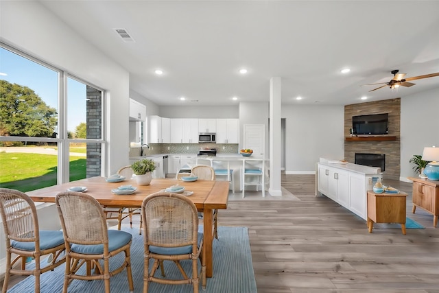 dining room featuring sink, a stone fireplace, light hardwood / wood-style floors, and ceiling fan