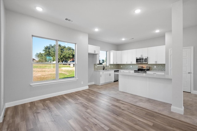 kitchen featuring sink, white cabinetry, light hardwood / wood-style flooring, appliances with stainless steel finishes, and backsplash