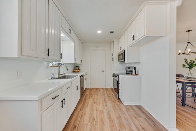 kitchen with sink, decorative light fixtures, light wood-type flooring, appliances with stainless steel finishes, and white cabinets