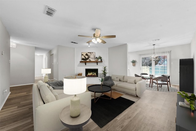 living room featuring a brick fireplace, ceiling fan with notable chandelier, and hardwood / wood-style flooring