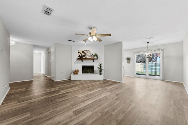 unfurnished living room featuring a fireplace, wood-type flooring, and ceiling fan with notable chandelier