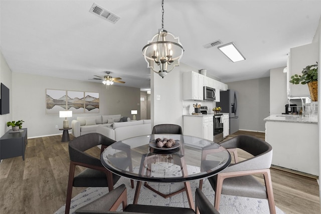 dining space with ceiling fan with notable chandelier and hardwood / wood-style flooring