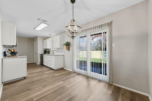 kitchen with a notable chandelier, white cabinets, sink, stainless steel dishwasher, and decorative light fixtures