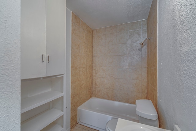 bathroom with tile patterned floors, toilet, tiled shower / bath combo, and a textured ceiling