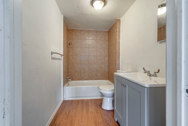 full bathroom featuring hardwood / wood-style floors, tiled shower / bath combo, vanity, toilet, and a textured ceiling