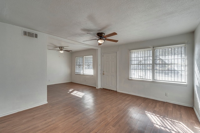 empty room featuring wood-type flooring, a healthy amount of sunlight, ceiling fan, and a textured ceiling